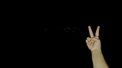 Close-up of hand gesturing against sky at night