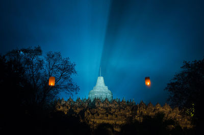 Illuminated trees and buildings against sky at night