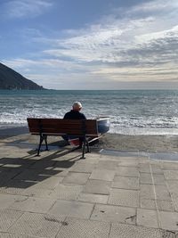 Rear view of man sitting on bench at beach