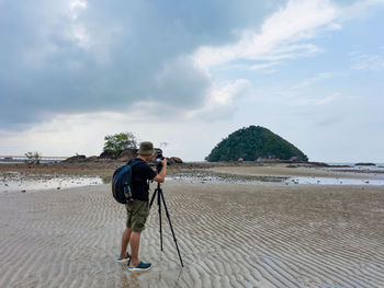 Rear view of man photograph the island or taking photo and standing on beach at low tide period.