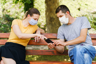 Portrait of man with woman using smart phone sitting on bench outdoors