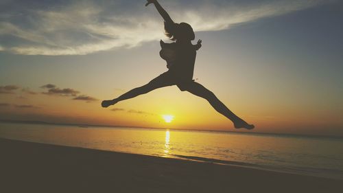 Silhouette carefree girl jumping at beach against sky during sunset