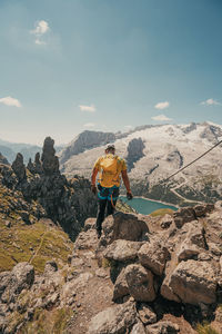 Man climbing on rock by mountain against sky