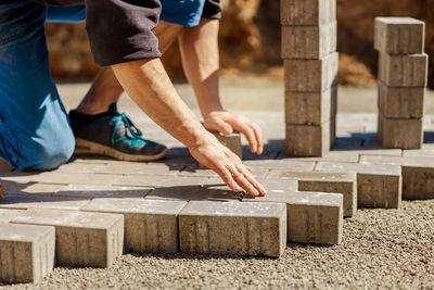 Young man laying gray concrete paving slabs in house courtyard on gravel foundation base. 