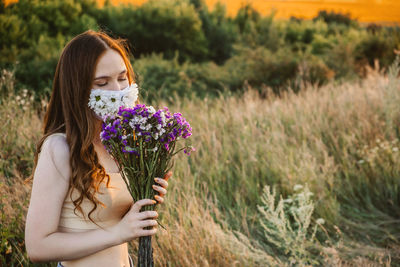 Low section of woman holding purple flowering plants on field