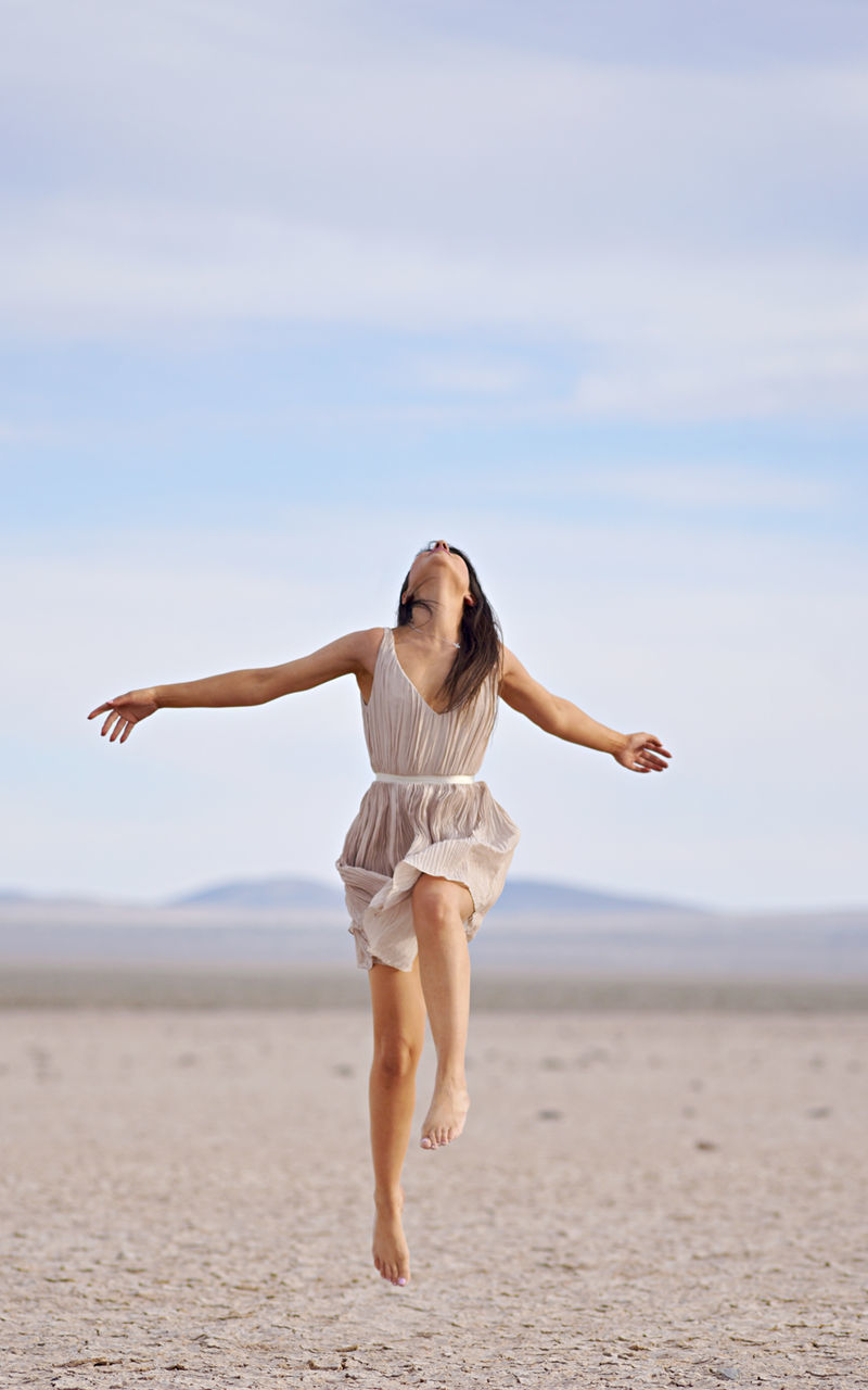 FULL LENGTH OF WOMAN WITH ARMS RAISED ON BEACH