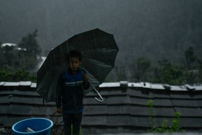 Rear view of boy standing in rain during rainy season