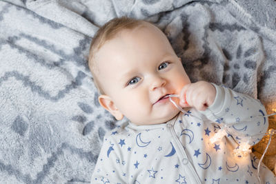 A baby boy lies on the bed and plays with a christmas garland.