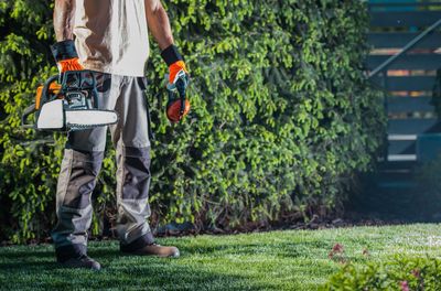 Low section of man holding gasoline chainsaw at yard