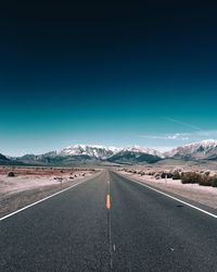 Empty road leading towards mountains against sky during winter