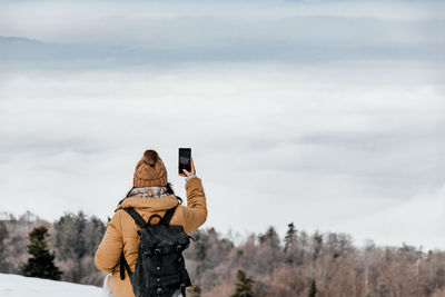 Rear view of young woman standing on top of hill and taking photos of valley. winter, fog.