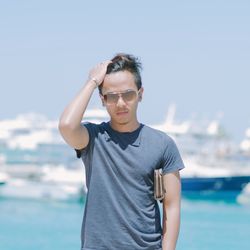 Man adjusting hair at sea shore against sky during sunny day