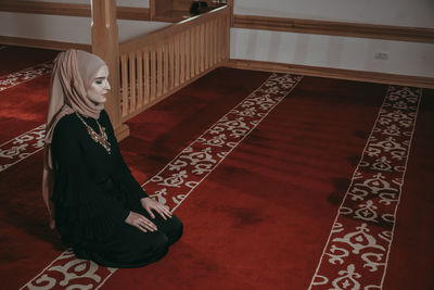 High angle view of woman praying while kneeling on carpet