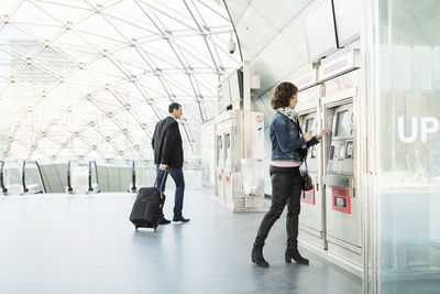 Businesswoman buying ticket while colleague walking at railroad station