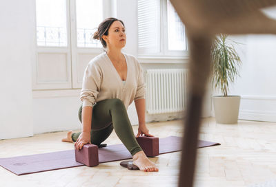 Attractive middle aged brunette woman in sportswear ptactice yoga with equipment in light studio