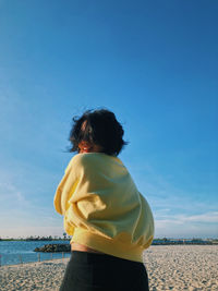 Rear view of woman standing on beach against clear blue sky