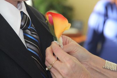 Cropped hands of woman attaching flower on suit for man during wedding