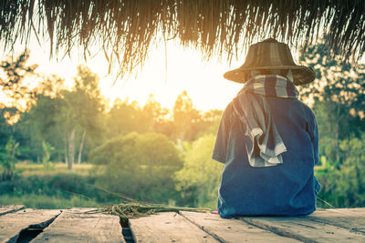 Rear view of person sitting on wooden plank