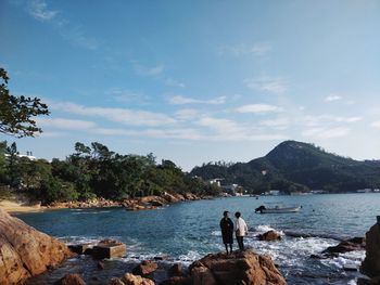 People on rocks by sea against sky