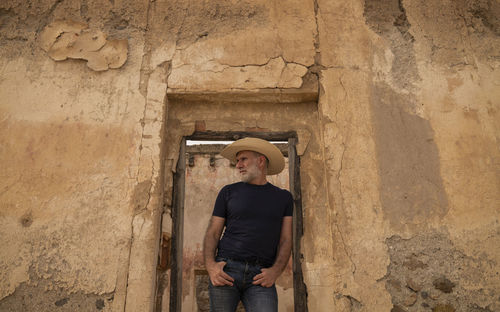 Adult man in cowboy hat standing on doorway of abandoned building