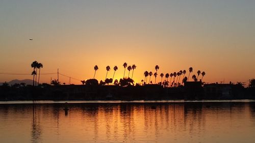 Silhouette palm trees by swimming pool against sky during sunset