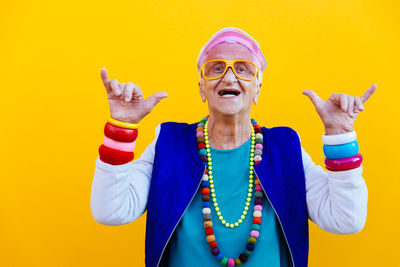 Portrait of senior woman wearing colorful jewelry standing against yellow background