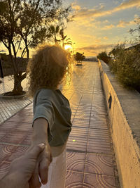 Rear view of woman walking on footbridge against sky during sunset