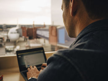 Rear view of mature man using laptop while sitting at airport