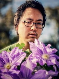 Close-up portrait of young man with large, purple clematis flowers.