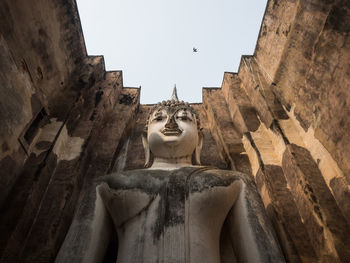 Low angle view of buddha statue on building against sky