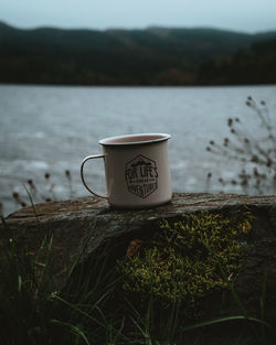 Travel inspirational camping mug on a rock near a river with moody mountains at loch in scotland.