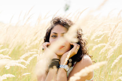 Portrait of smiling young woman with hand on chin sitting amidst plants during sunny day