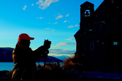 Man photographing by building against sky