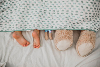 Low section of person by stuffed toys on bed at home