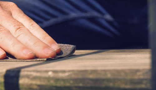 Midsection of carpenter sanding wooden plank at carpentry