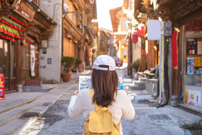 Rear view of woman standing on street amidst buildings in city