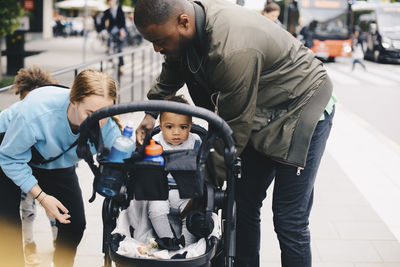 Parents with toddler by baby stroller on sidewalk in city