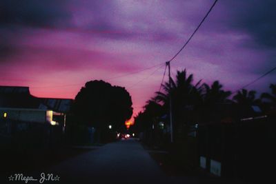 Road by silhouette trees against sky at sunset