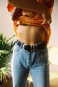 Midsection of sensuous woman removing t-shirt while standing agaisnt plant and wall