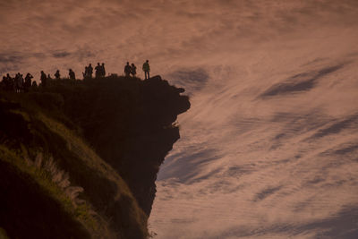 Low angle view of people at cliff against cloudy sky