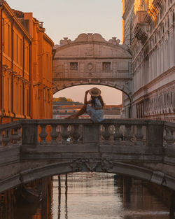 Full length of woman sitting on bridge over canal