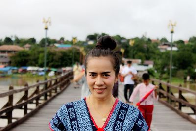 Portrait of woman standing on railing in city against sky