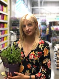 Portrait of beautiful woman with potted plant standing in store