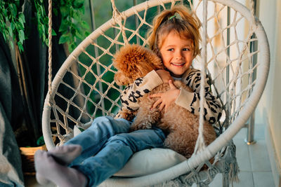 Happy little girl, child hugging with a smile her pet, poodle dog at home on the balcony in spring