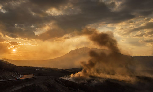 Smoke emitting from volcanic mountain against sky during sunset