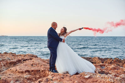 Rear view of couple holding hands at beach against sky