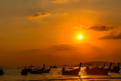 Silhouette boats moored in sea against orange sky