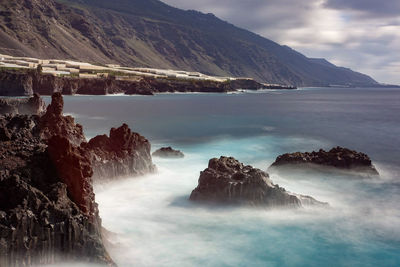 Scenic view of sea by mountain against sky