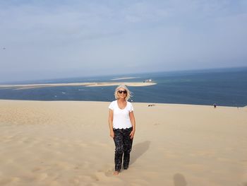 Portrait of woman wearing sunglasses while standing at beach against sky