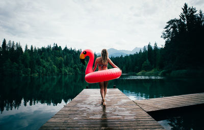 Woman on pier by lake against sky